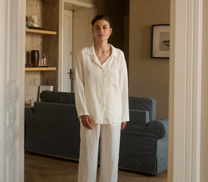 Model wearing a relaxed nightwear set in lightweight milky white linen, featuring a long-sleeve button-up shirt and wide-leg pants