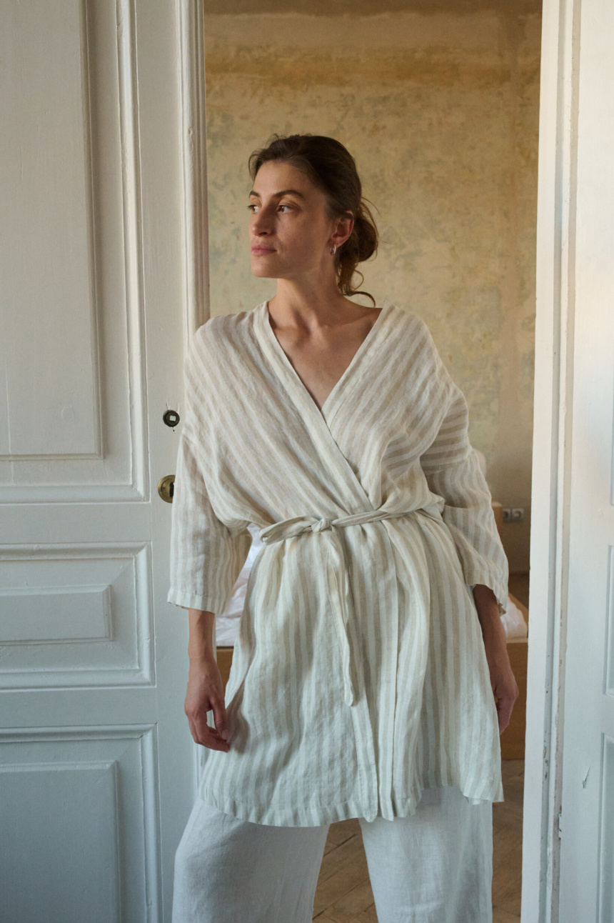 Model wearing a natural stripes linen robe with a belt, paired with white pants, all in lightweight linen for a relaxed and comfortable look