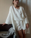 Woman wearing an all-white lightweight linen outfit consisting of a loose-fitting sleeveless top, shorts, and an short open robe