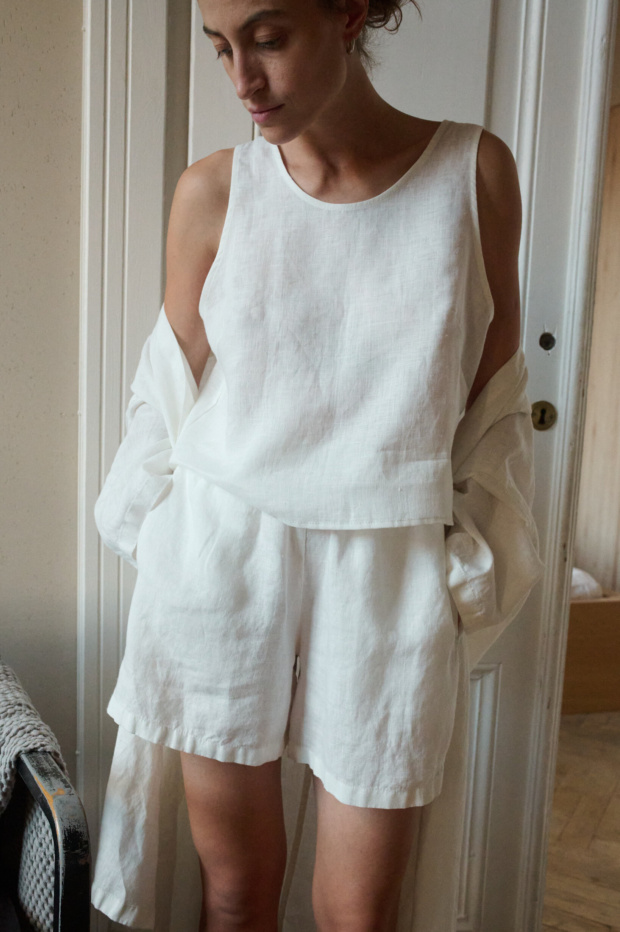 Woman in a relaxed white linen outfit, including a sleeveless top and matching shorts, as well as a lightweight linen robe