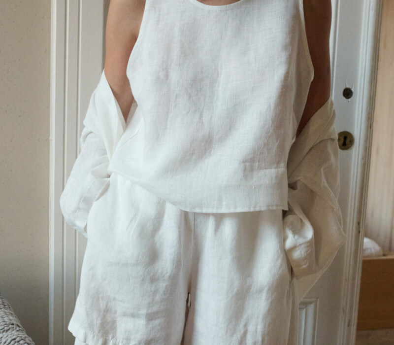 Woman in a relaxed white linen outfit, including a sleeveless top and matching shorts, as well as a lightweight linen robe