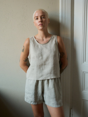 Model wearing a sleeveless top in natural grey linen with a rounded neckline and cropped length, paired with matching shorts, creating a relaxed loungewear look