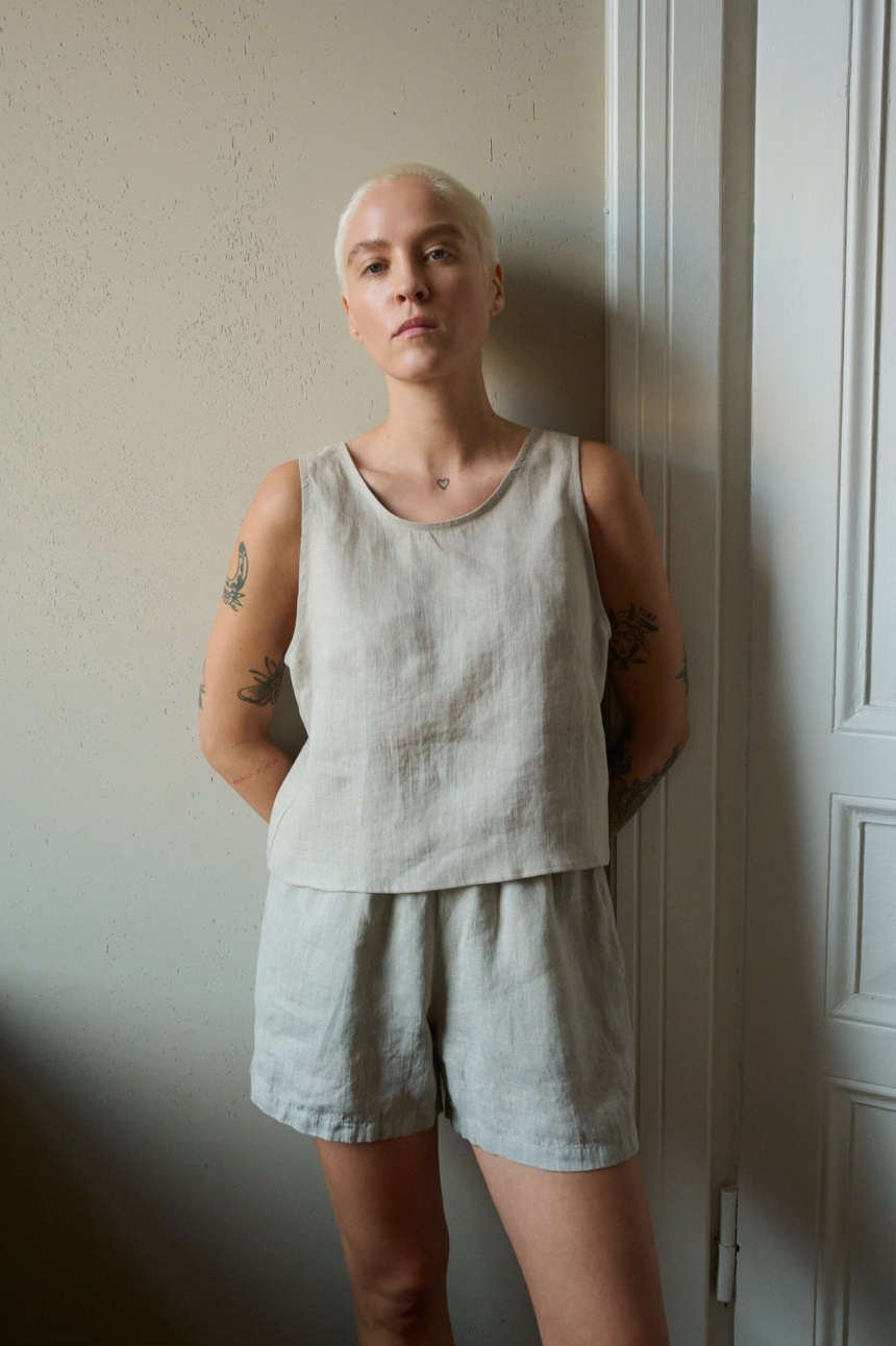 Model wearing a sleeveless top in natural grey linen with a rounded neckline and cropped length, paired with matching shorts, creating a relaxed loungewear look