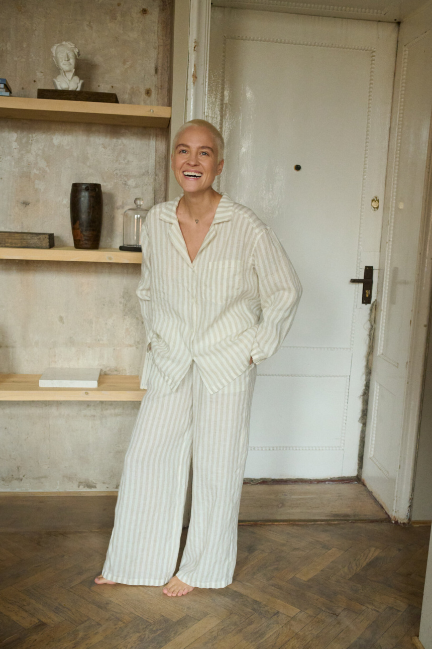 Woman laughing and posing in white and natural grey linen pajama trousers with pockets and long sleeved linen shirt with V-neckline. Breathable and light linen fabric is made for lounging and relaxing at home or beyond.