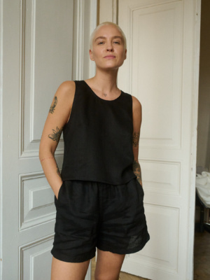 Model wearing a black sleeveless top and matching shorts in lightweight linen, with the shorts featuring pockets