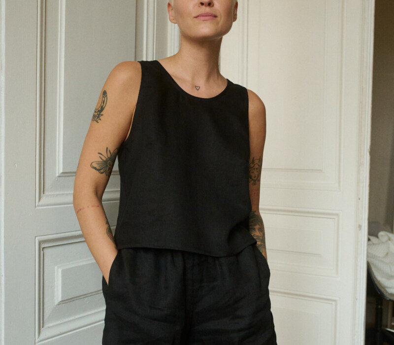 Model wearing a black sleeveless top and matching shorts in lightweight linen, with the shorts featuring pockets