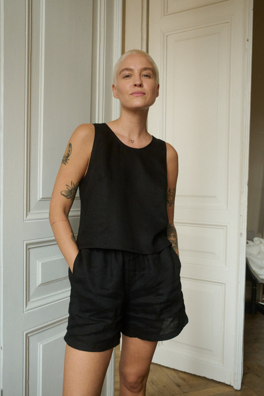 Model wearing a black sleeveless top and matching shorts in lightweight linen, with the shorts featuring pockets