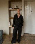 Model wearing a two-piece black lightweight linen set, consisting of a relaxed button-up shirt with a single chest pocket and coordinating wide-leg pants