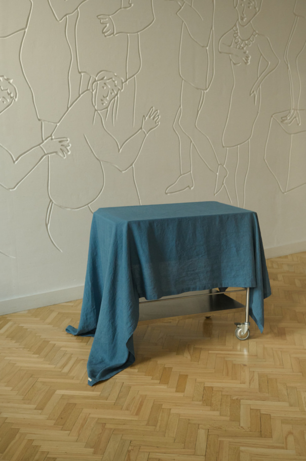 linen tablecloth in blue draped over a metal table with wheels against an artistic wall