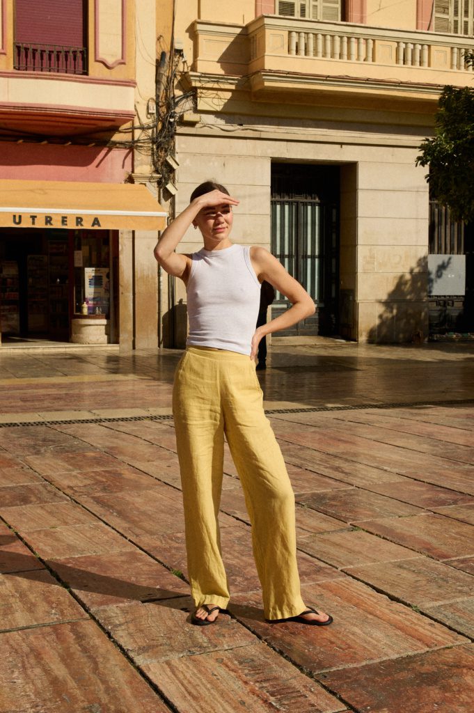 Model wearing a white fitted tank top paired with butter yellow wide leg linen pants featuring an elasticated waist and side pockets