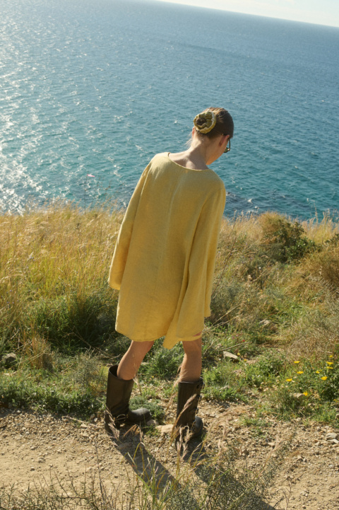 Model shown from the back, wearing a butter-colored mini linen dress in a relaxed, oversized fit with long sleeves