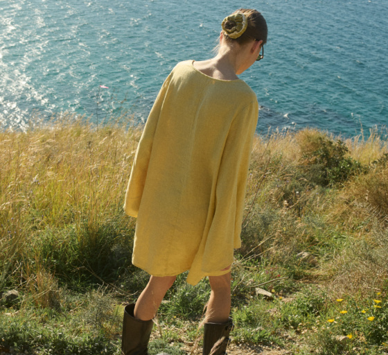 Model shown from the back, wearing a butter-colored mini linen dress in a relaxed, oversized fit with long sleeves