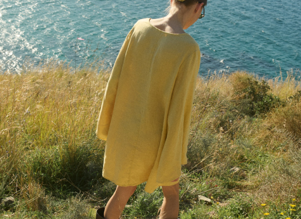 Model shown from the back, wearing a butter-colored mini linen dress in a relaxed, oversized fit with long sleeves