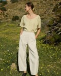 Woman wearing a flowing light yellow checkered linen button-up blouse with short sleeves and a scoop neck, tucked into high-waisted natural grey wide-leg pants