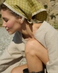 Model wearing a linen bandana in a pickle checks pattern with white lace trim, tied around the head, paired with a natural cotton blend dress