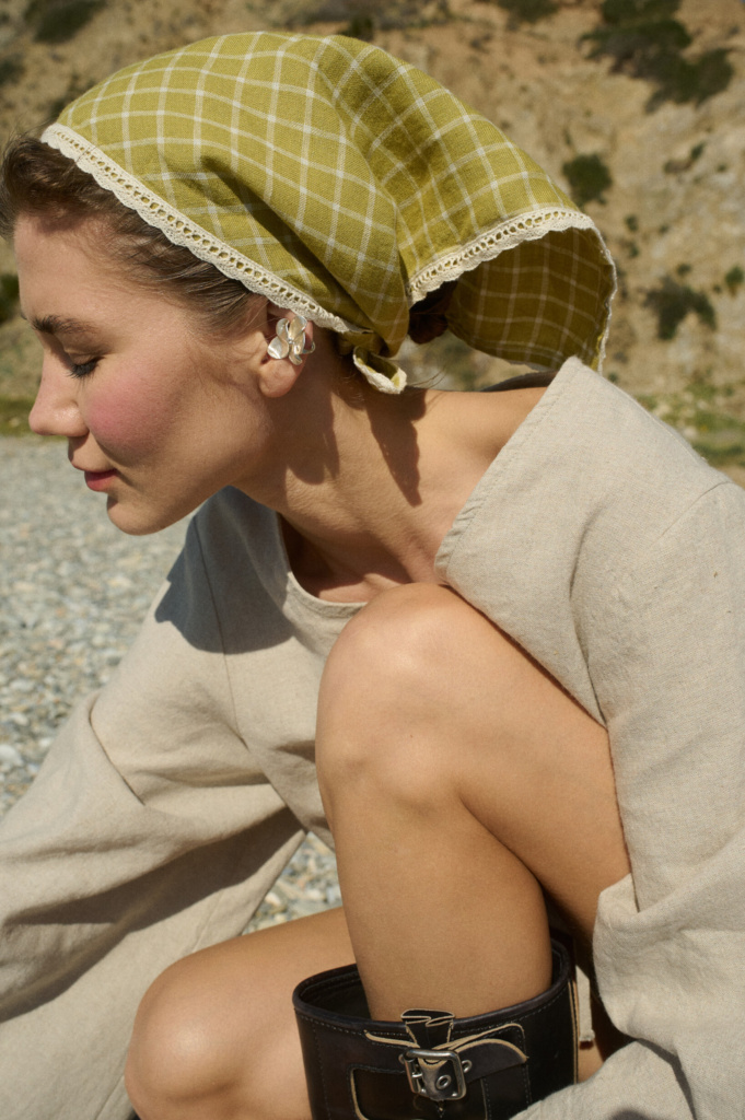 Model wearing a linen bandana in a pickle checks pattern with white lace trim, tied around the head, paired with a natural cotton blend dress