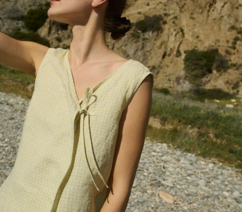 Model wearing a sleeveless V-neck checkered top, designed with a delicate side tie and a relaxed fit that drapes effortlessly