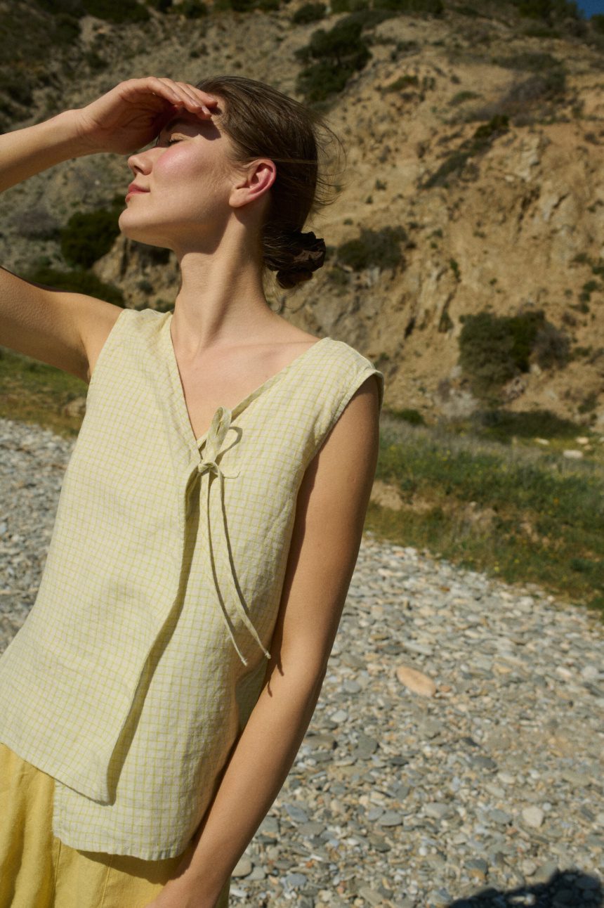 Model wearing a sleeveless V-neck checkered top, designed with a delicate side tie and a relaxed fit that drapes effortlessly