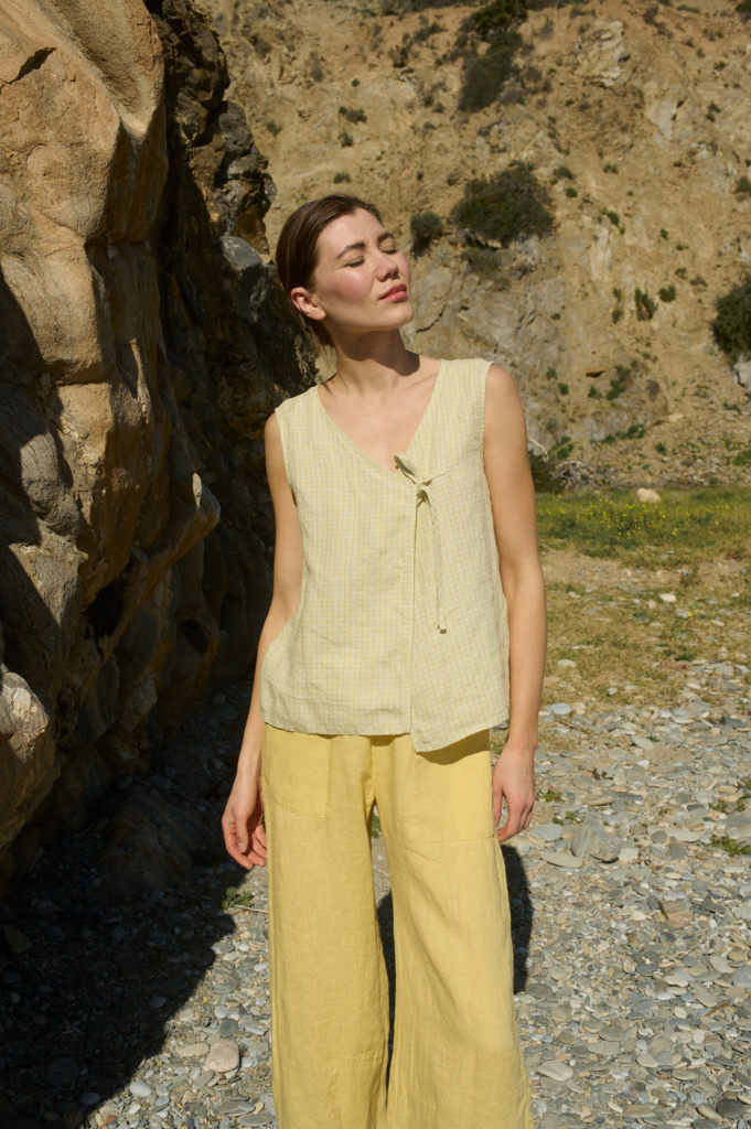 Model wearing a sleeveless V-neck top in soft apple checks linen, featuring a delicate side tie and a relaxed, airy fit, paired with matching wide-leg butter yellow linen pants