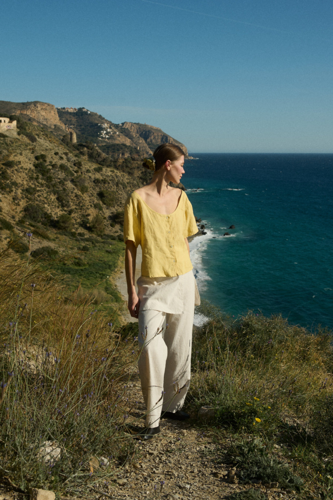 Model in a loose-fitting butter-yellow linen button-up top with a scoop neckline, paired with flowy white wide-leg pants that feature a unique skirt panel detail