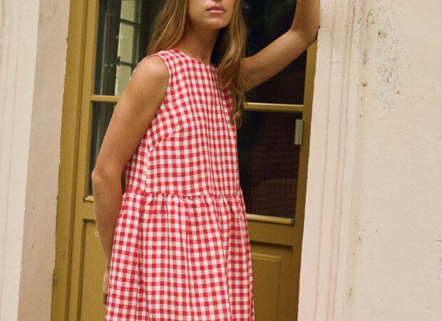 Woman wearing a sleeveless red and white gingham linen dress with a gathered, midi-length skirt.
