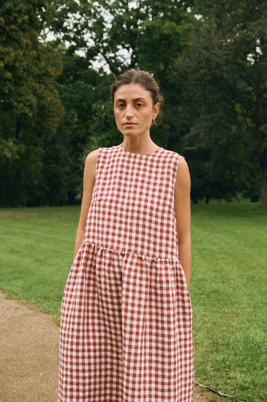 Model in a sleeveless terracotta gingham linen dress with a relaxed drop waist and functional side pockets.