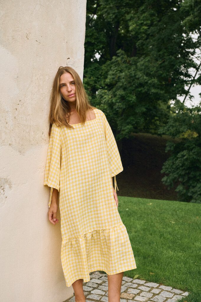 A woman wearing a yellow gingham linen dress in nature.