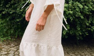 Model wearing an off-white linen midi dress with wide sleeves and ruffle hem, side view highlighting the natural linen drape