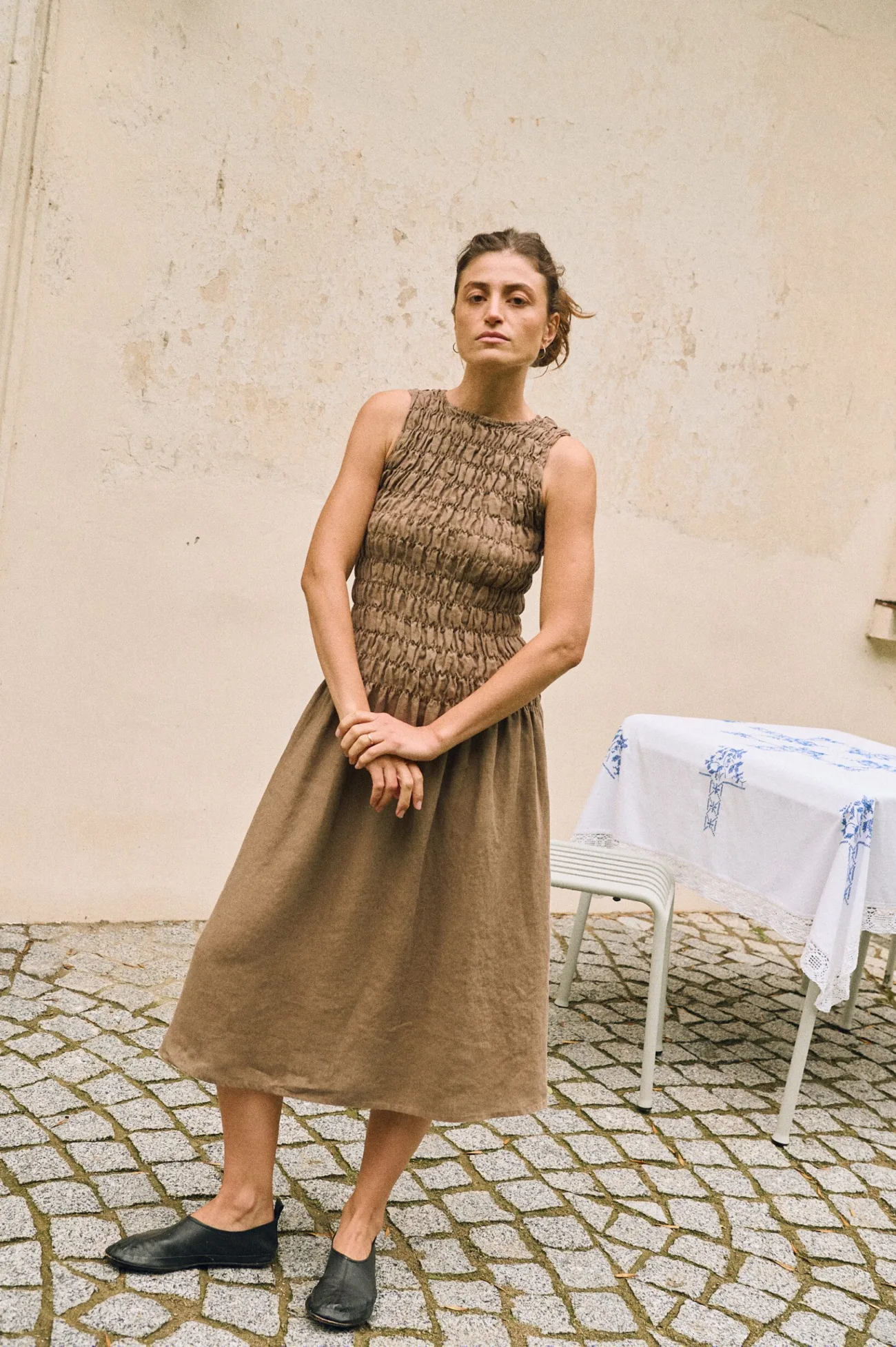 Model wearing a sleeveless cacao linen dress with smocked bodice and midi length