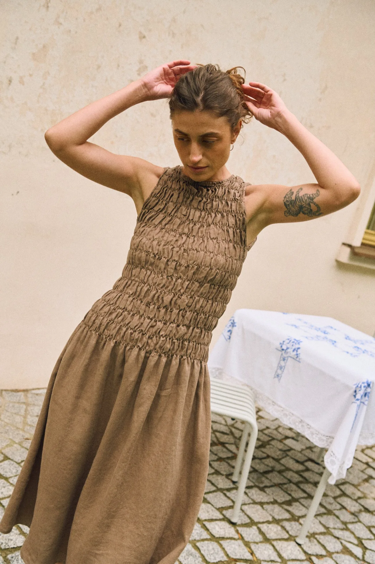 Model wearing sleeveless cacao linen dress with smocked bodice and flowing midi skirt