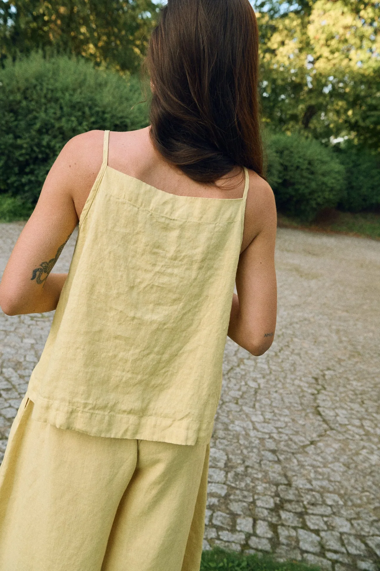 Back view of butter yellow linen camisole top with straight neckline and thin straps, paired with wide-leg linen trousers