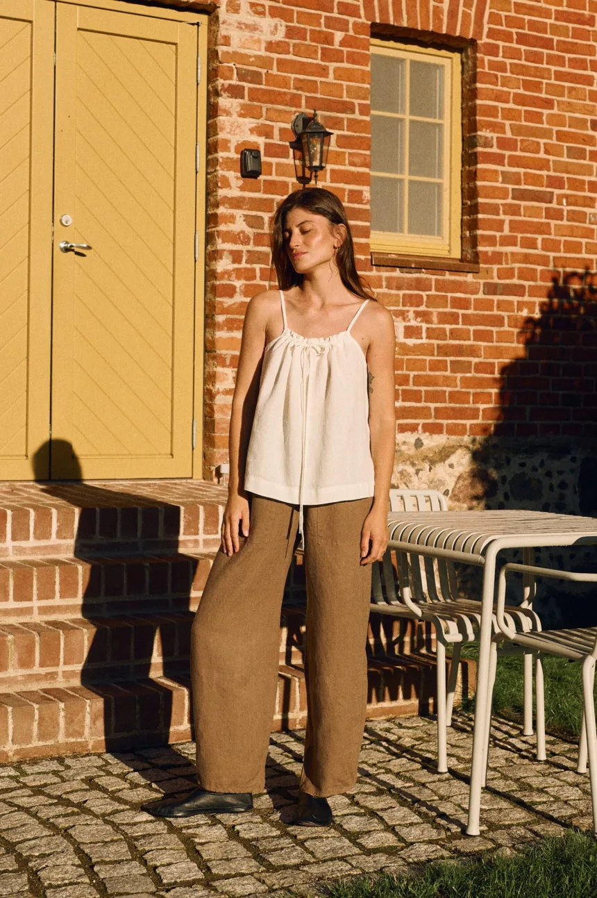 Milky white linen cami with gathered neckline styled with high-waisted cacao linen trousers with barrel leg silhouette