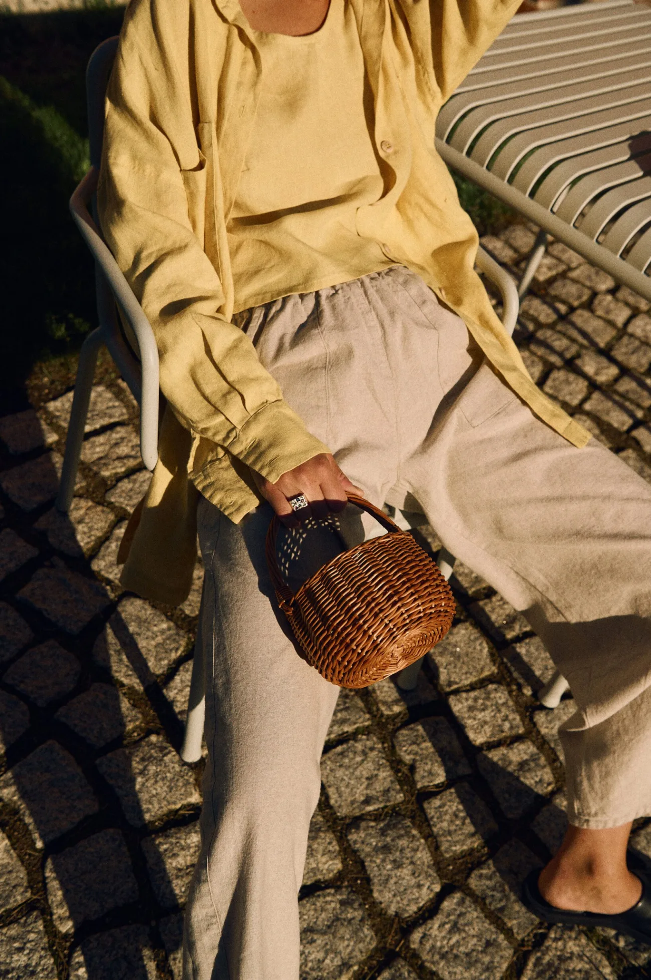 Natural cotton-linen blend trousers styled with butter yellow linen tank and oversized shirt, seated view