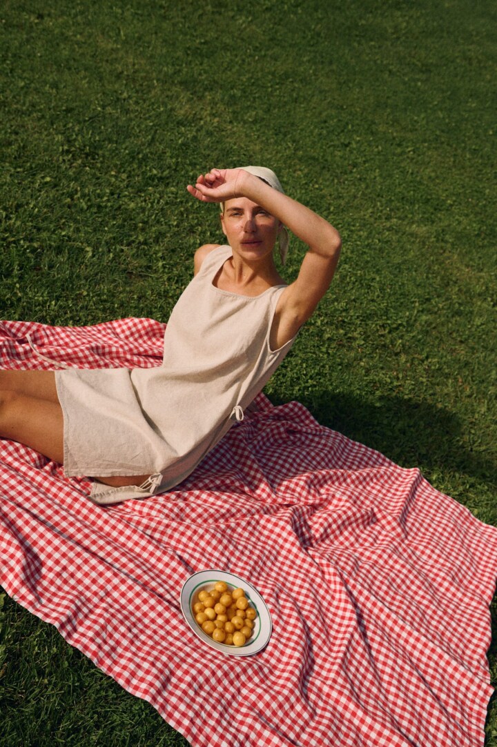 Model wearing a sleeveless natural cotton blend summer dress with side tie details, styled outdoors on a picnic blanket