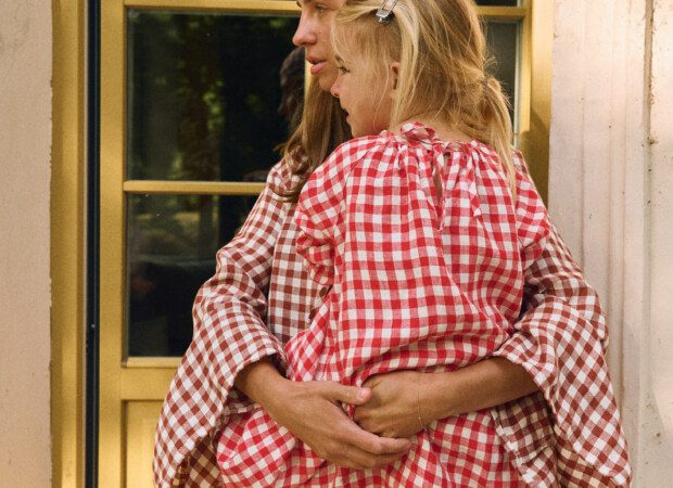 Woman wearing terracotta gingham linen dress holding child in red gingham linen dress