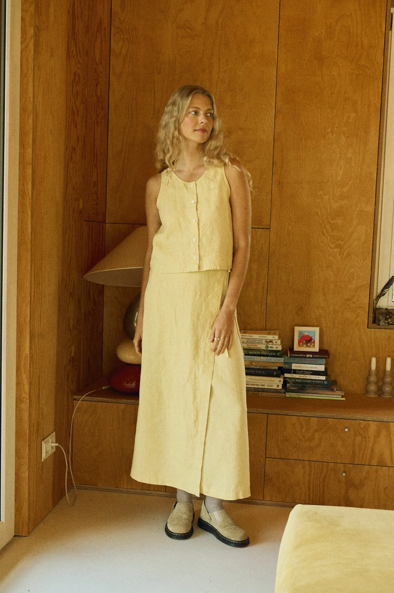 Woman wearing a sleeveless button-up top and a matching ankle-length wrap skirt, both in butter-colored linen