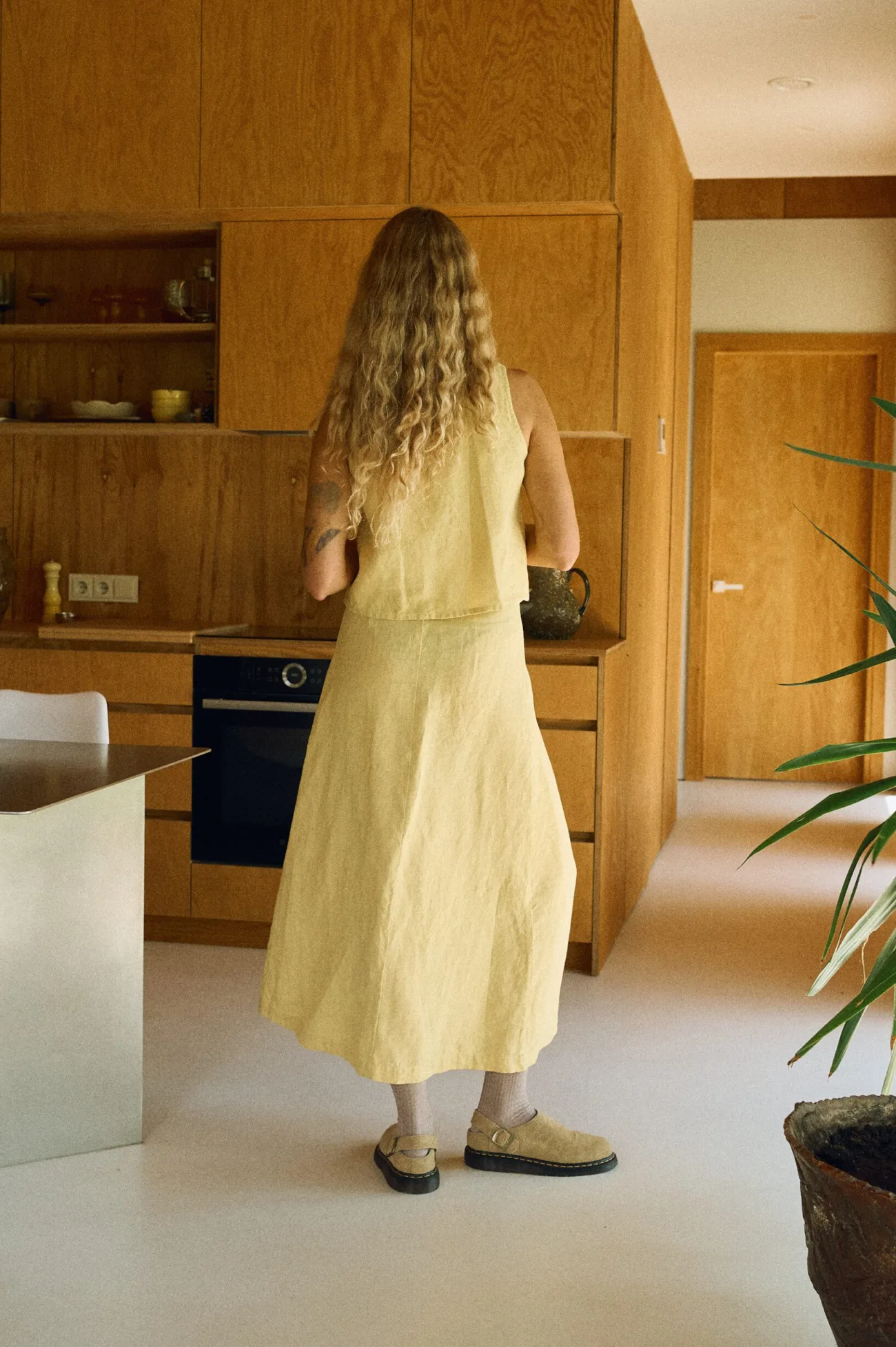 Back view of a woman wearing a butter-colored linen sleeveless top and matching ankle-length wrap skirt