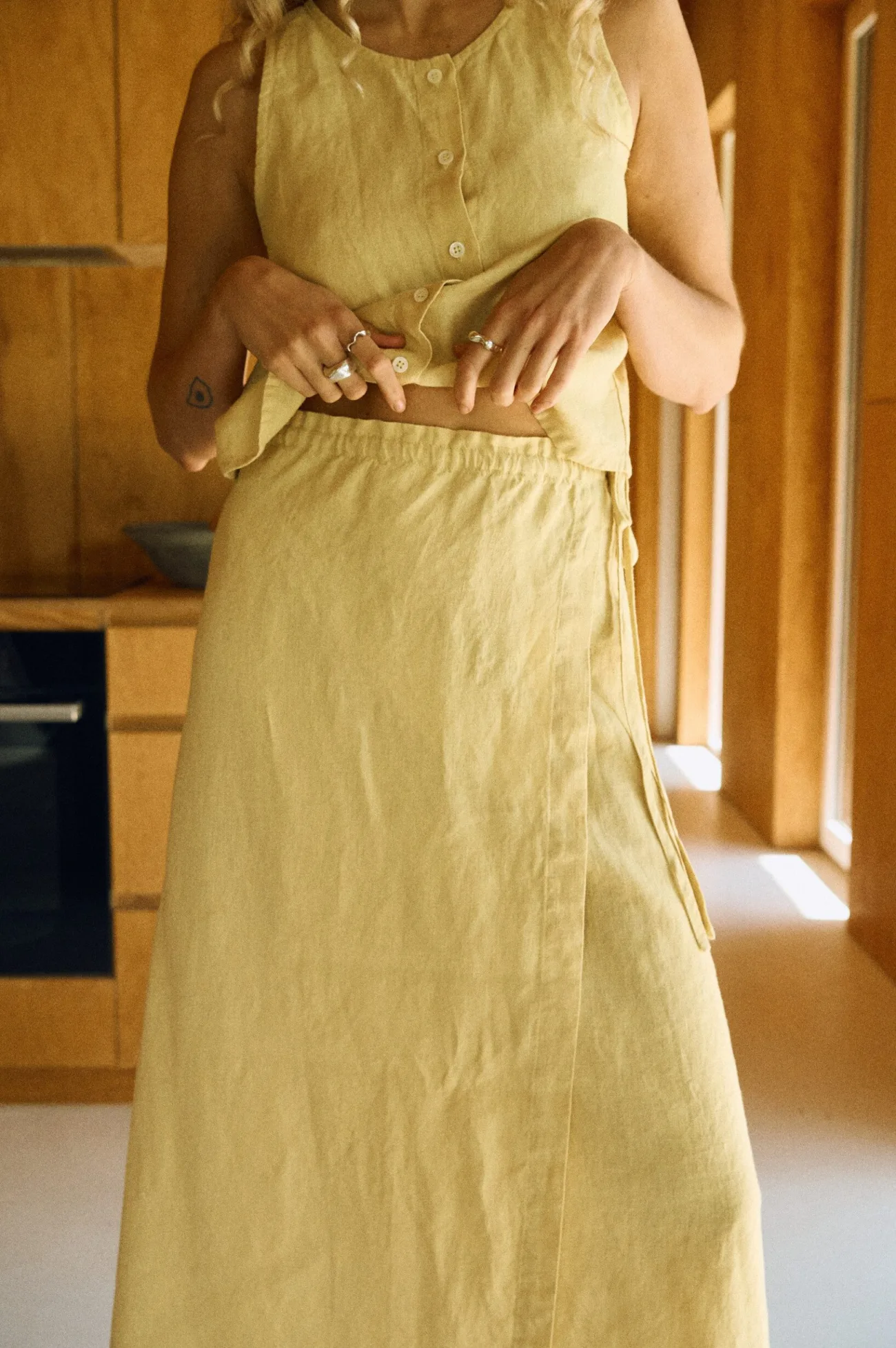 Close-up of a woman wearing a butter-colored medium weight linen wrap skirt with a flat front and long adjustable side ties
