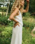 Side view of a woman wearing a white linen sleeveless top paired with a matching white linen wrap skirt