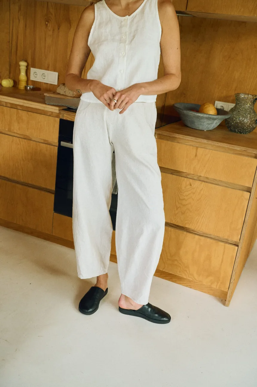 Woman wearing a milky white linen sleeveless button-up top and wide-leg trousers