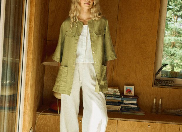 Woman wearing an olive green belted linen overshirt made from heavy linen, styled over a white sleeveless top and white wide-leg linen-cotton pants