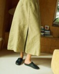 Close-up of a high-waisted olive green midi skirt made from heavy linen, featuring a front slit, belt loops, and a structured A-line cut