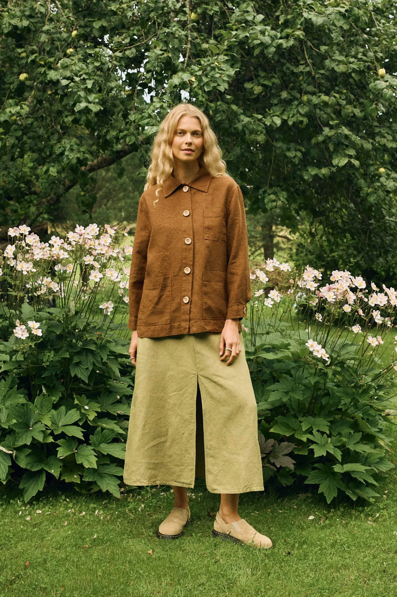 Front view of a warm brown linen-wool blend jacket with large natural buttons and patch pockets, styled with a heavy linen A-line skirt in olive green featuring a front slit