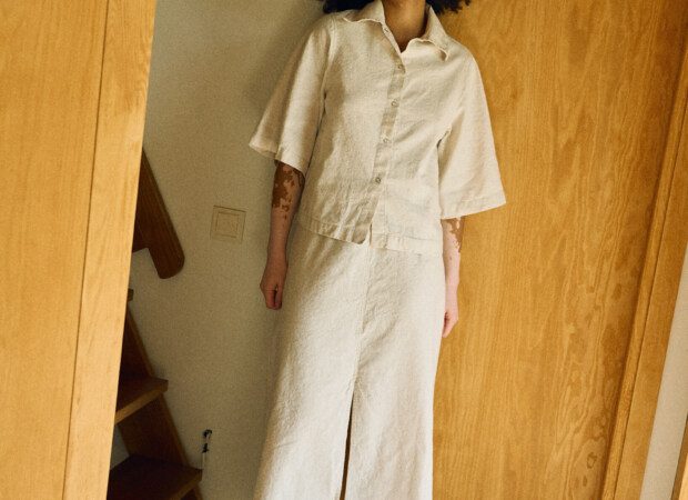 Full front view of a neutral-toned linen-cotton outfit featuring a short-sleeve collared button-up shirt paired with a high-waisted midi skirt with a front slit