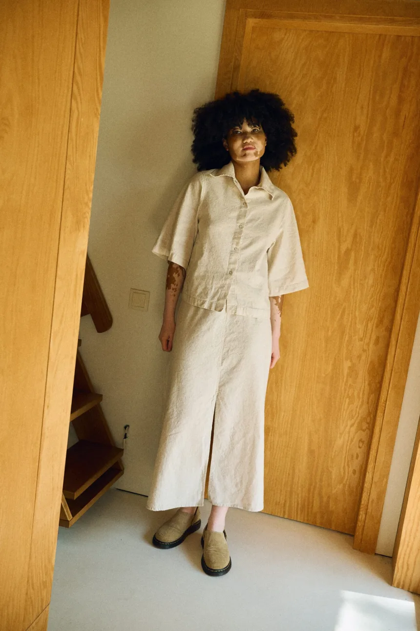 Woman wearing a matching natural-colored linen-cotton blend outfit featuring a short-sleeve button-up shirt and a high-waisted midi skirt with front slit