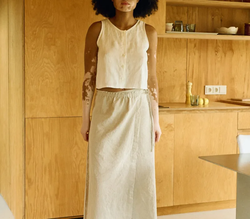 Woman wearing a natural cotton-linen blend ankle-length wrap skirt with a clean A-line silhouette, flat front, and long adjustable ties, paired with a sleeveless button-up top