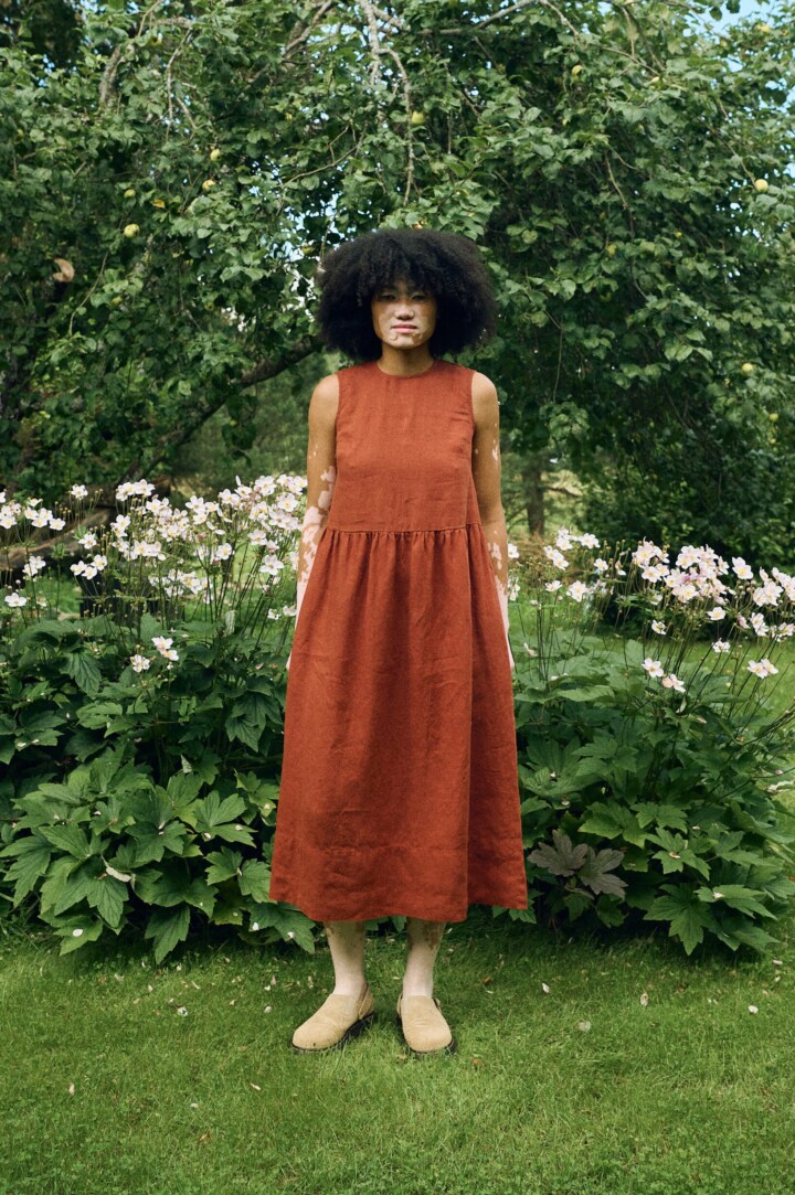 Sleeveless midi dress in terracotta linen featuring a high round neckline, fitted bodice, gathered waist, and a softly flared skirt