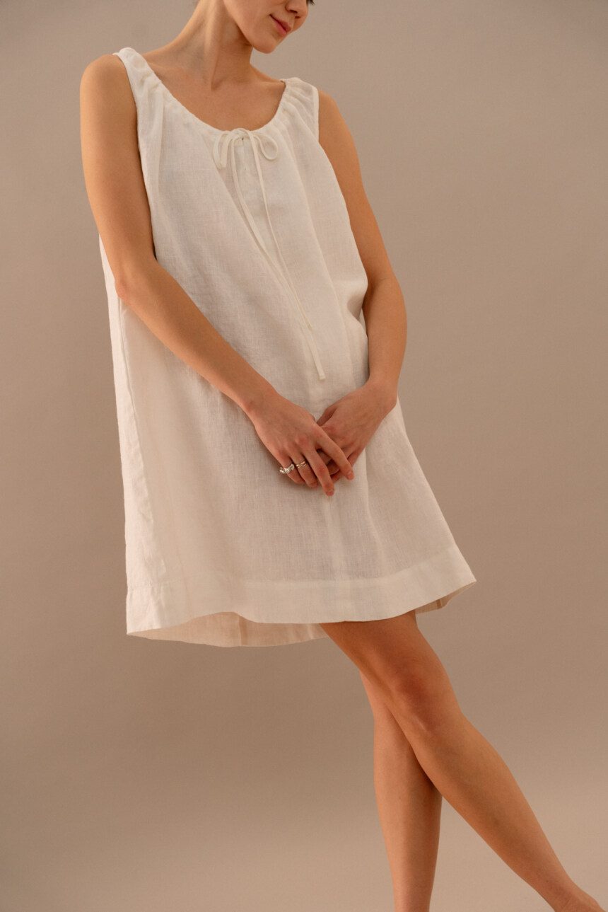 Close-up of white linen dress featuring gathered neckline and bow tie closure