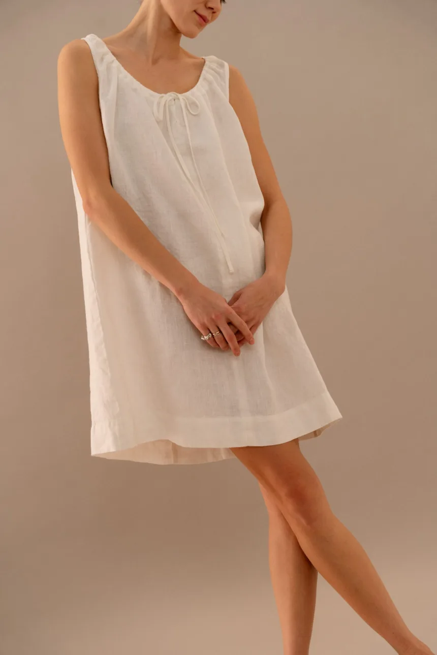 Close-up of white linen dress featuring gathered neckline and bow tie closure