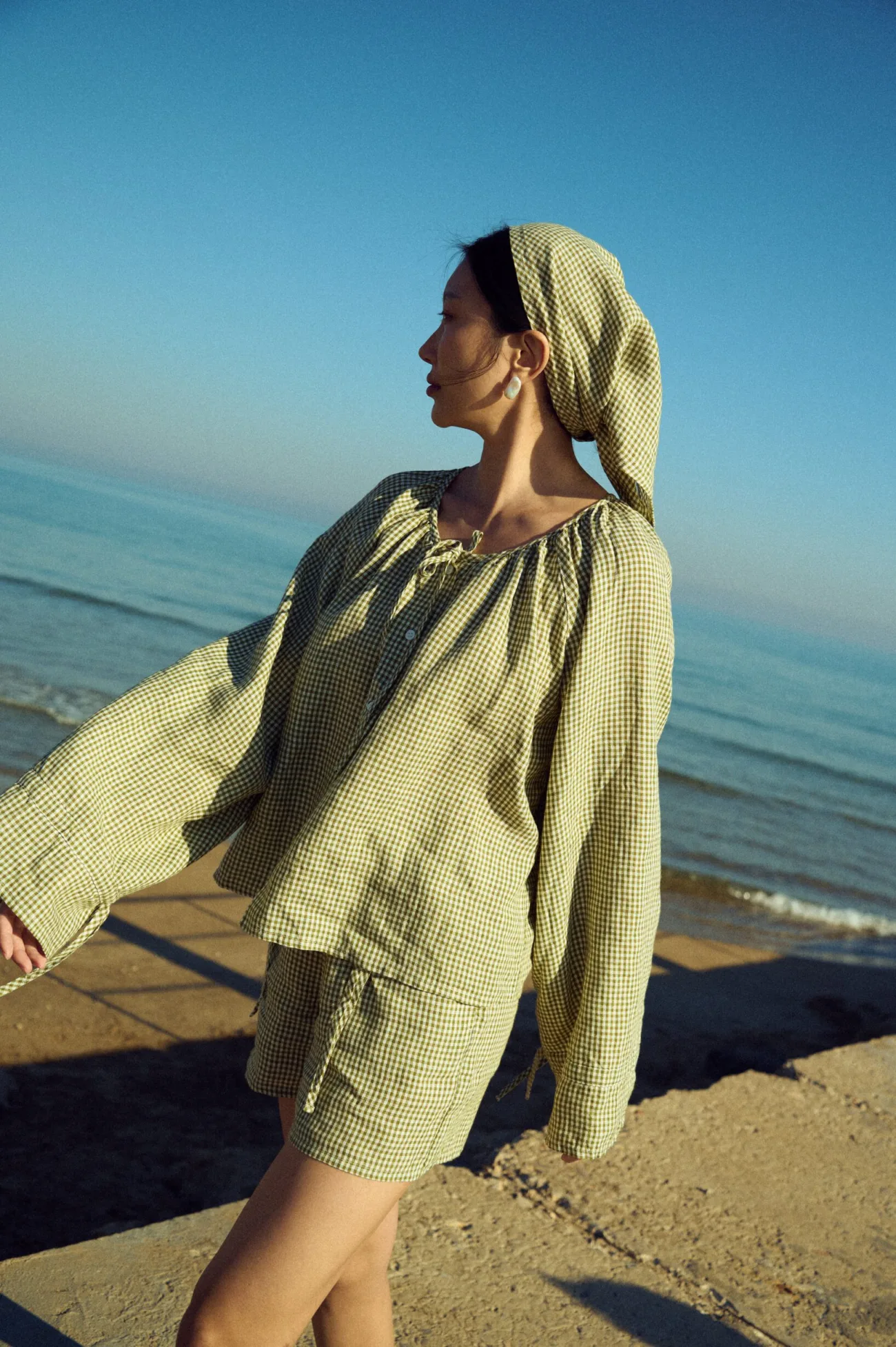 Moss green gingham triangle scarf worn as a head covering with a loose blouse and coordinating shorts set